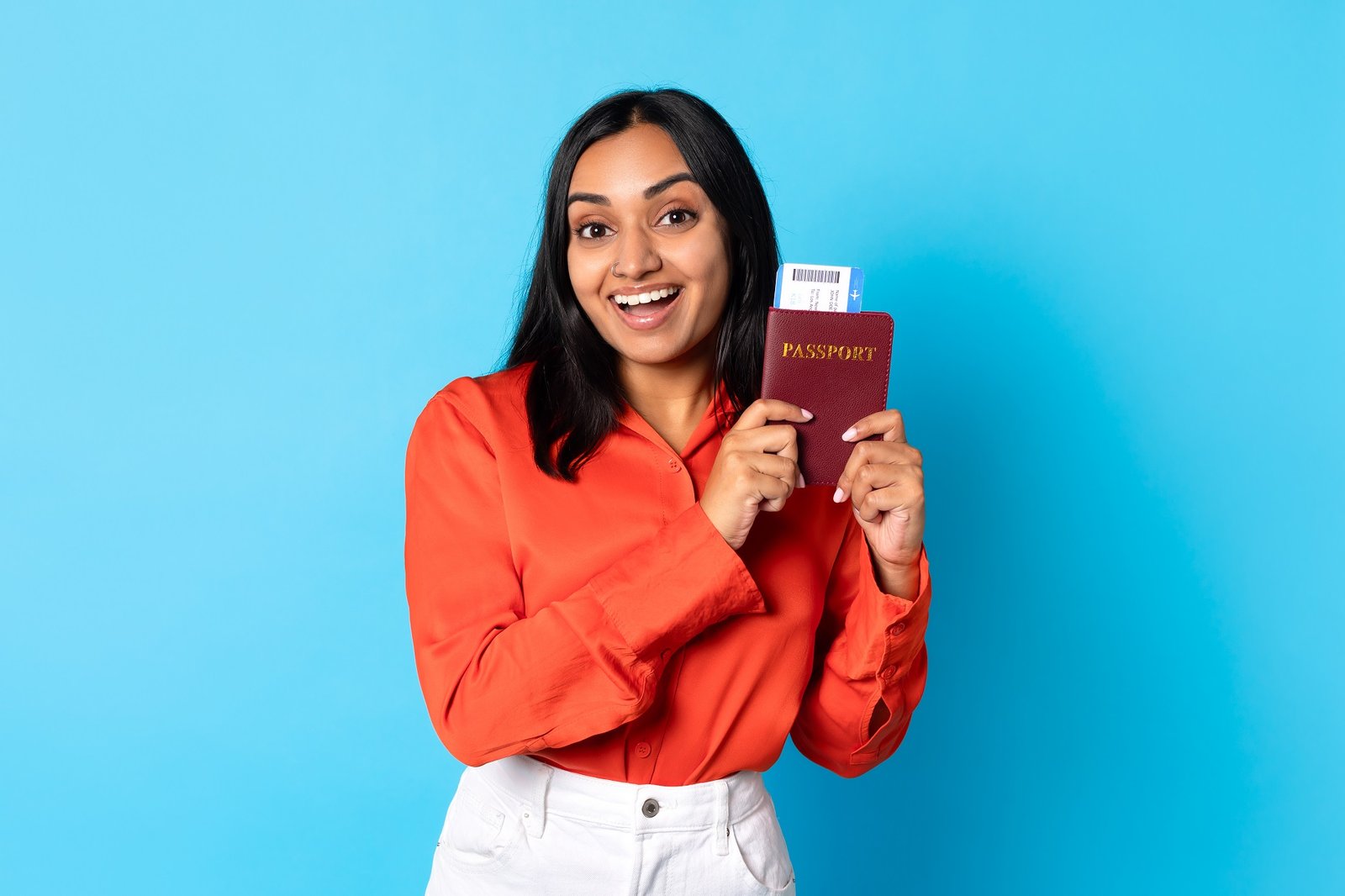 Happy young indian lady traveler showing passport and boarding pass in blue studio, smiling to camera and promoting travel offer for millennials, modern holiday advertisement banner